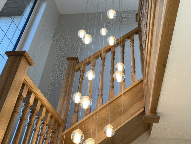 Multiple multi-level hanging lights in the center of a wooden staircase